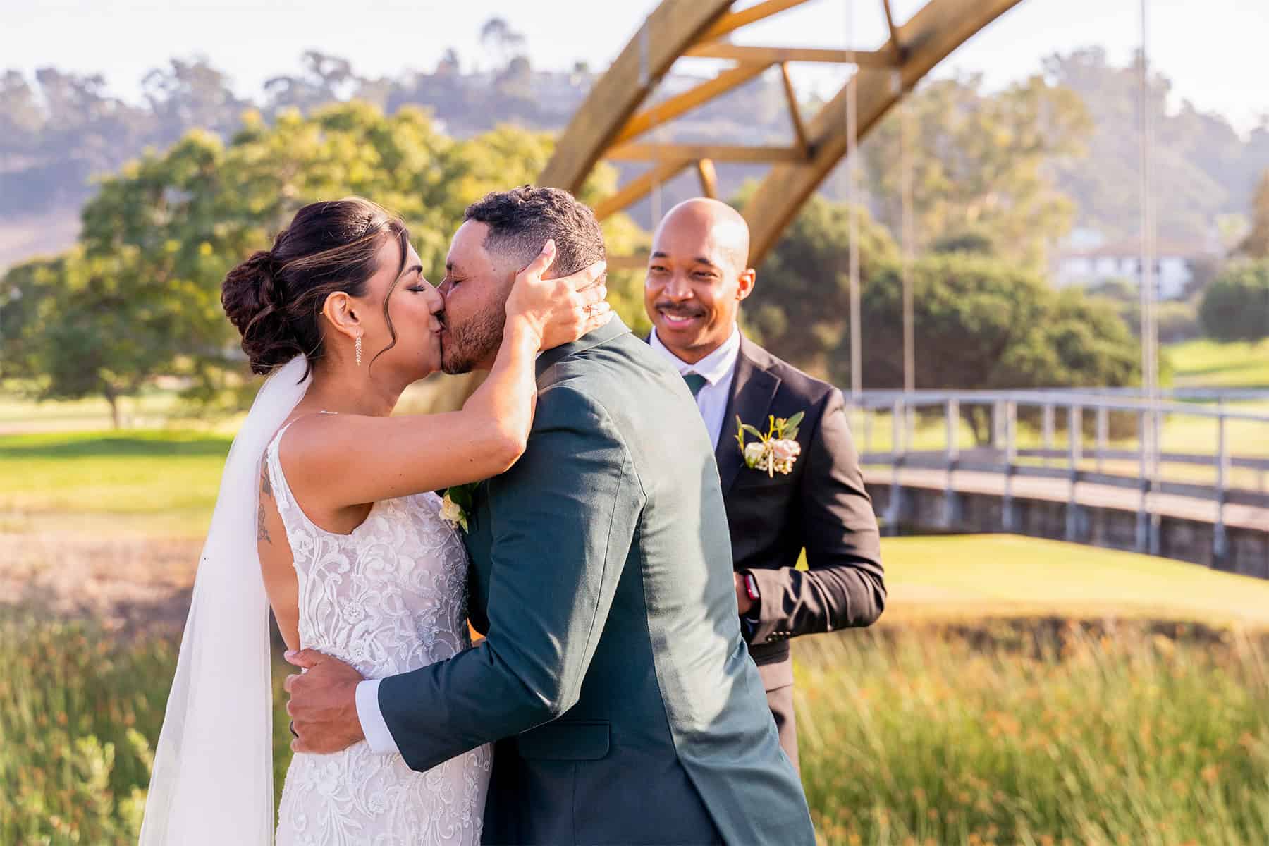 bride-groom-wedding-kiss-san-diego-riverwalk-golf-club-bridge Bride and groom kiss Riverwalk Golf Club bridge and nature backdrop at San Diego outdoor wedding
