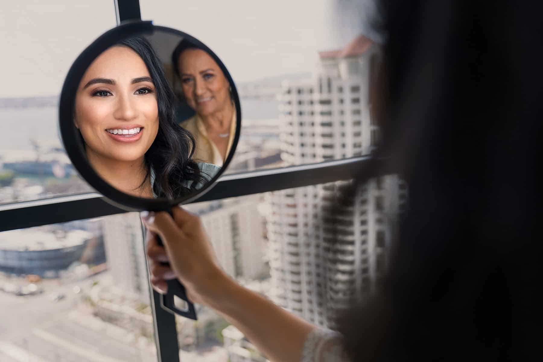 bride-with-mother-mirror-reflection-downtown-san-diego-wedding Mother and bride share a joyful moment captured through a mirror at San Diego wedding