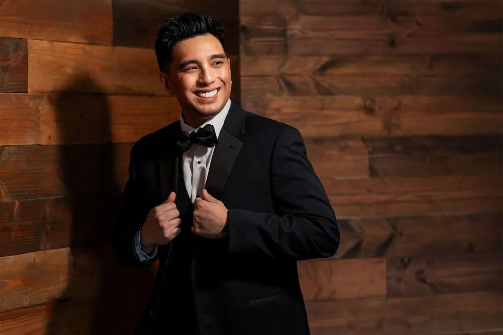 Groom in black tuxedo smiling while adjusting bow tie before San Diego wedding ceremony