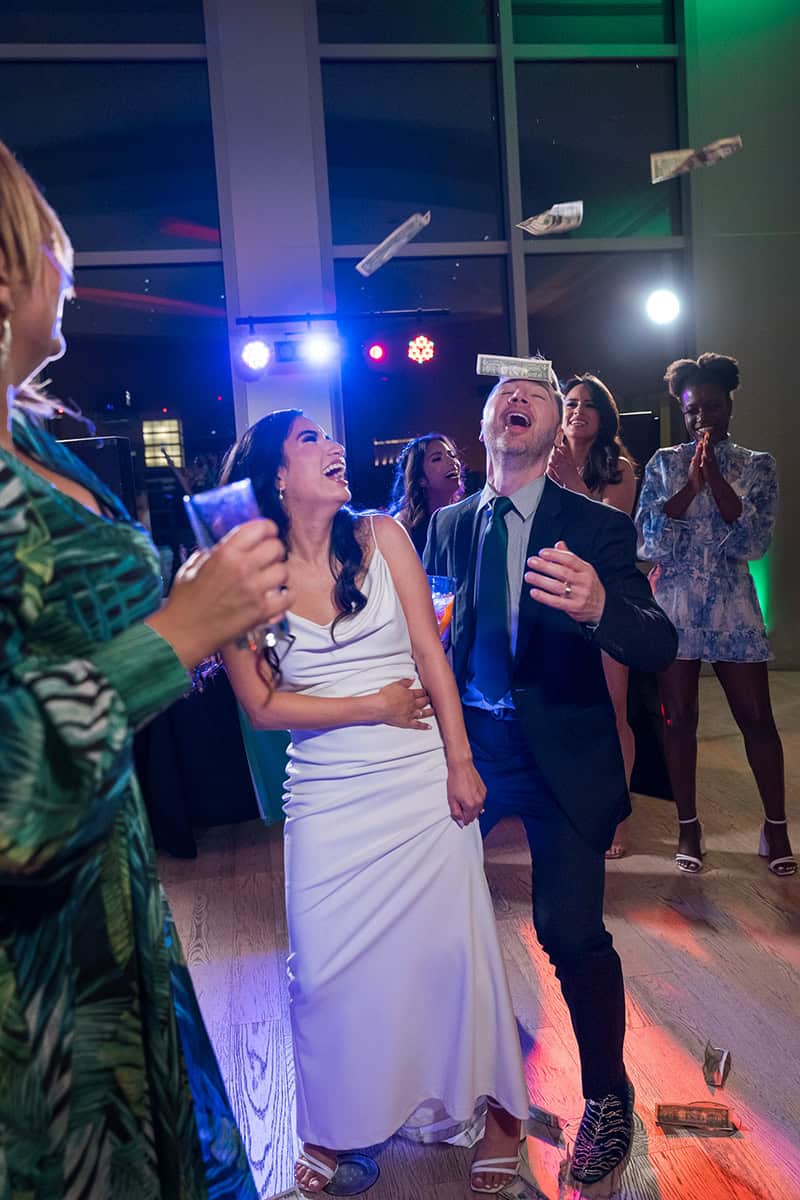 wedding-dance-floor-money-dance-celebration-skybox-san-diego Bride and groom celebrate with laughter and dollar bills flying on the dance floor at a San Diego Skybox wedding