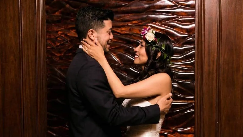 Happy couple dancing together at wedding celebration with floral crown and elegant wooden backdrop in San Diego