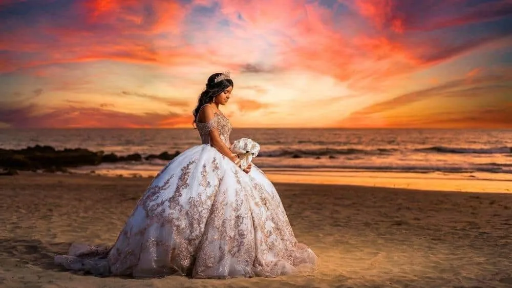 Quinceanera photo idea featuring an elegant gown against a colorful beach sunset