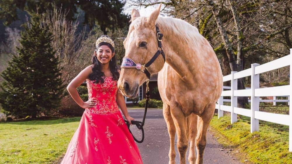 Quinceanera photo idea showcasing a girl in an elegant gown standing beside a horse