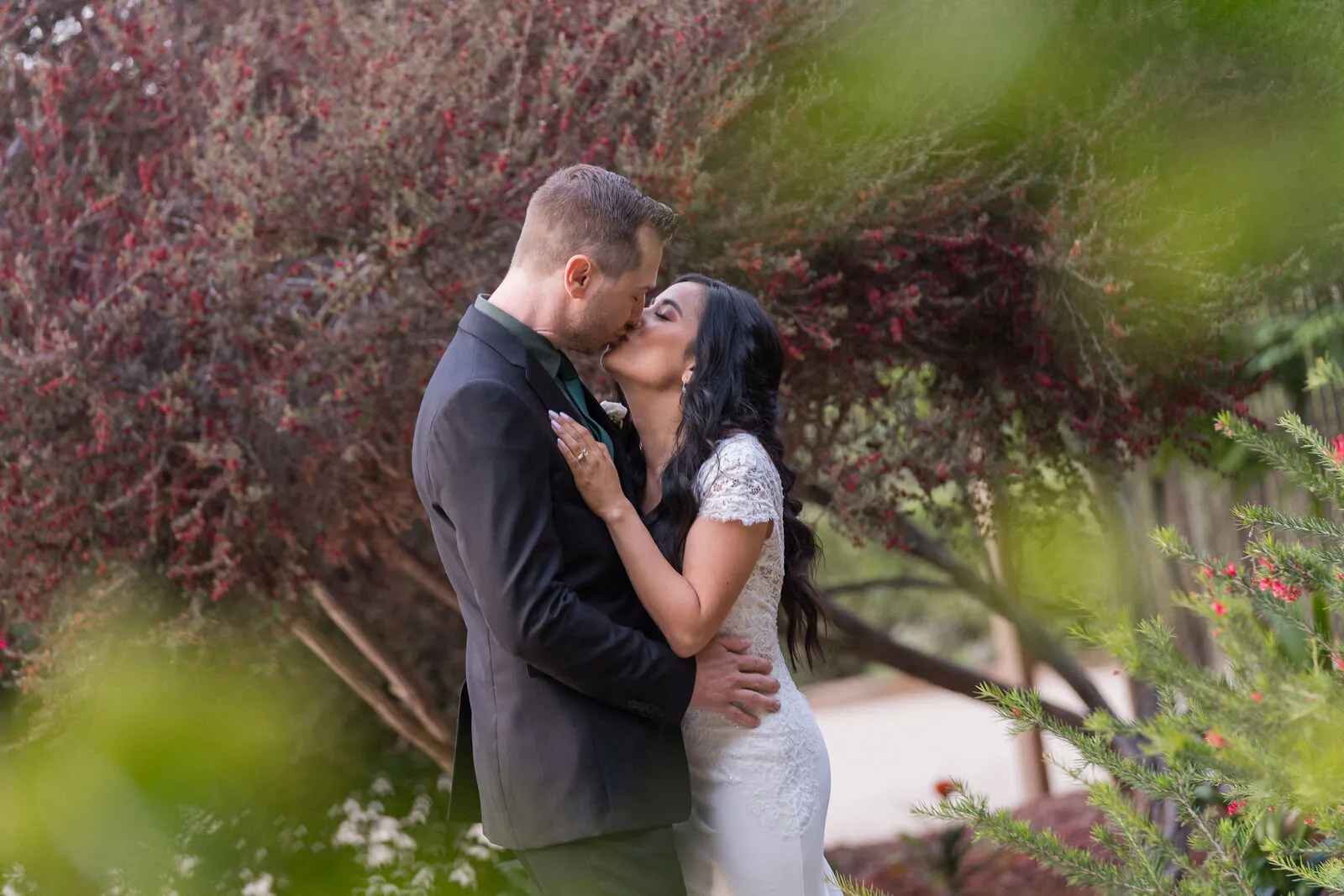 Engaged couple kissing in lush garden with red ivy and green foliage, romantic engagement photography moment