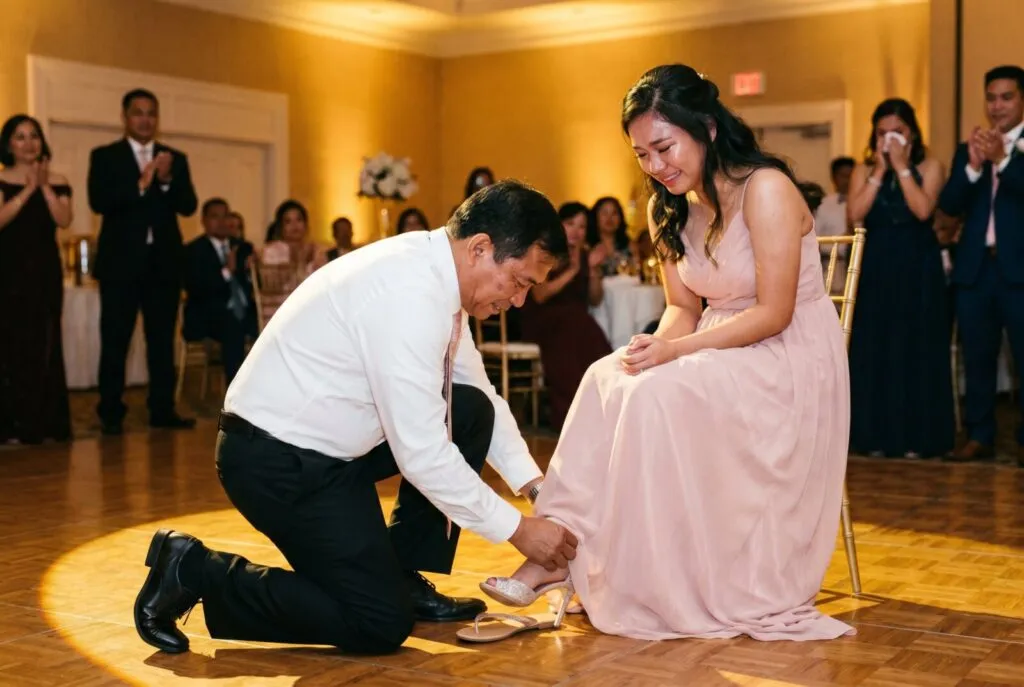 Groom kneeling to remove garter during Filipino debut dance celebration in San Diego ballroom with guests watching