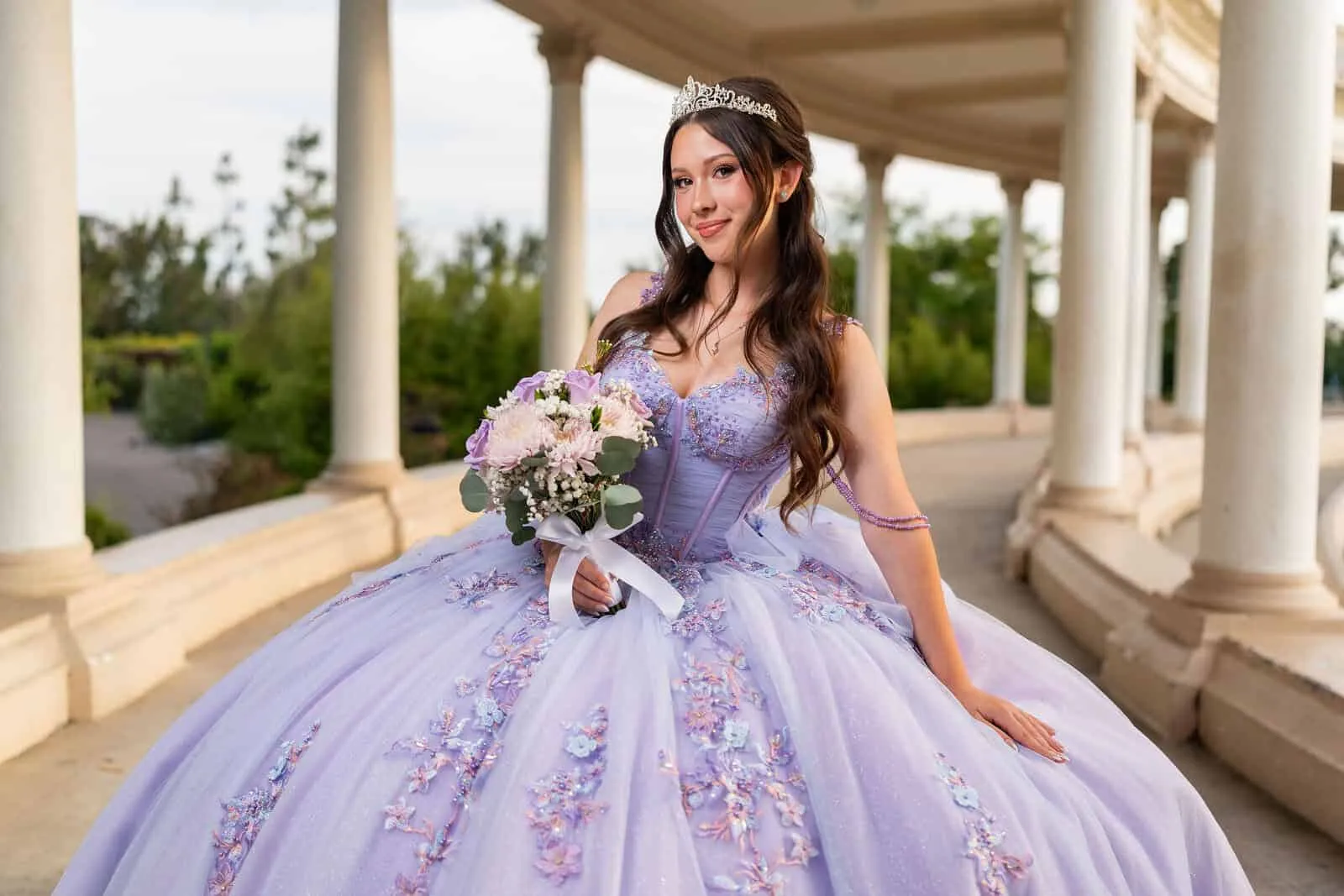 Young woman in elegant lavender quinceanera dress with floral embroidery, tiara, and bouquet poses under classical columns for San Diego portrait photography