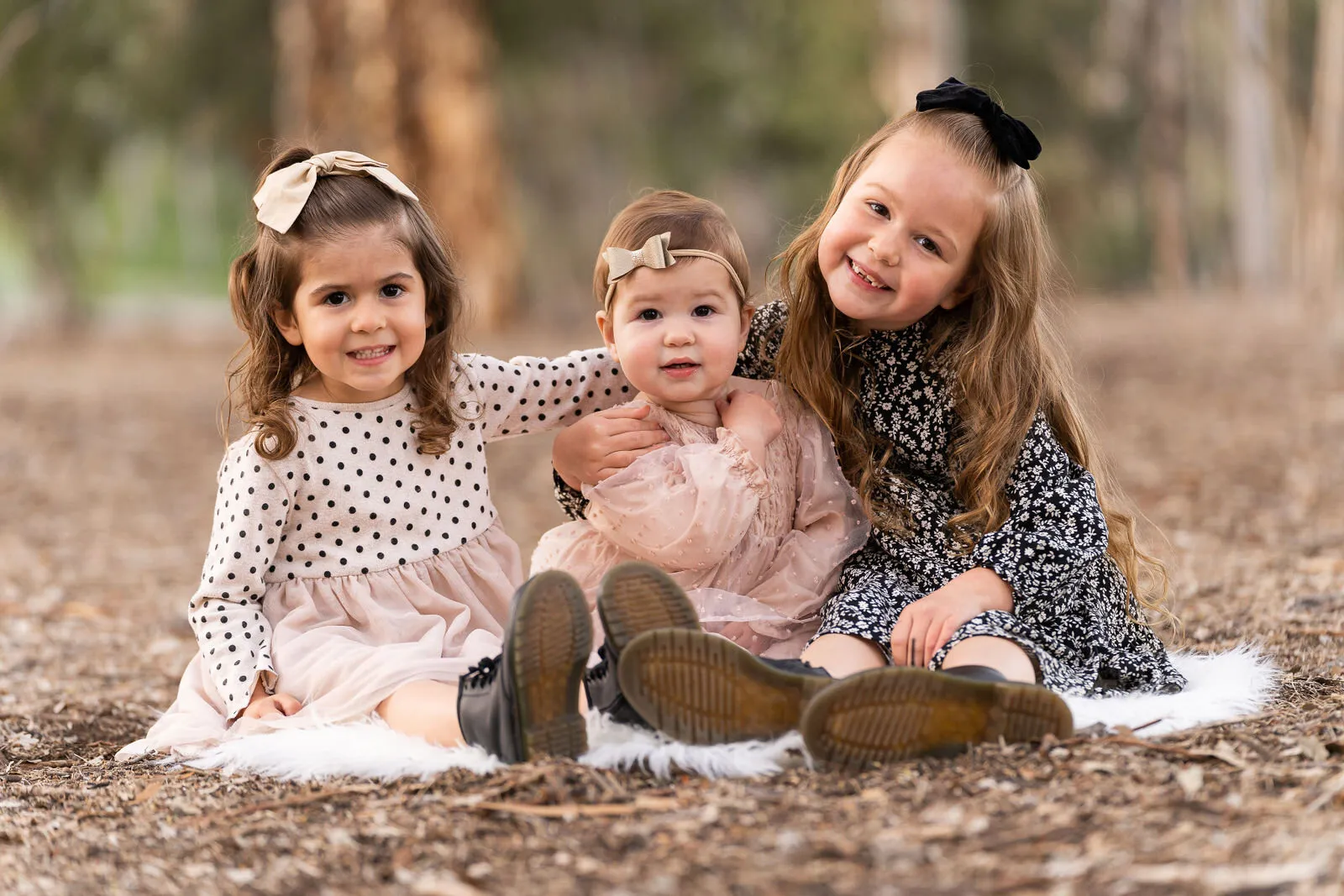 Three young girls smiling together outdoors in San Diego family portrait photography session with natural background